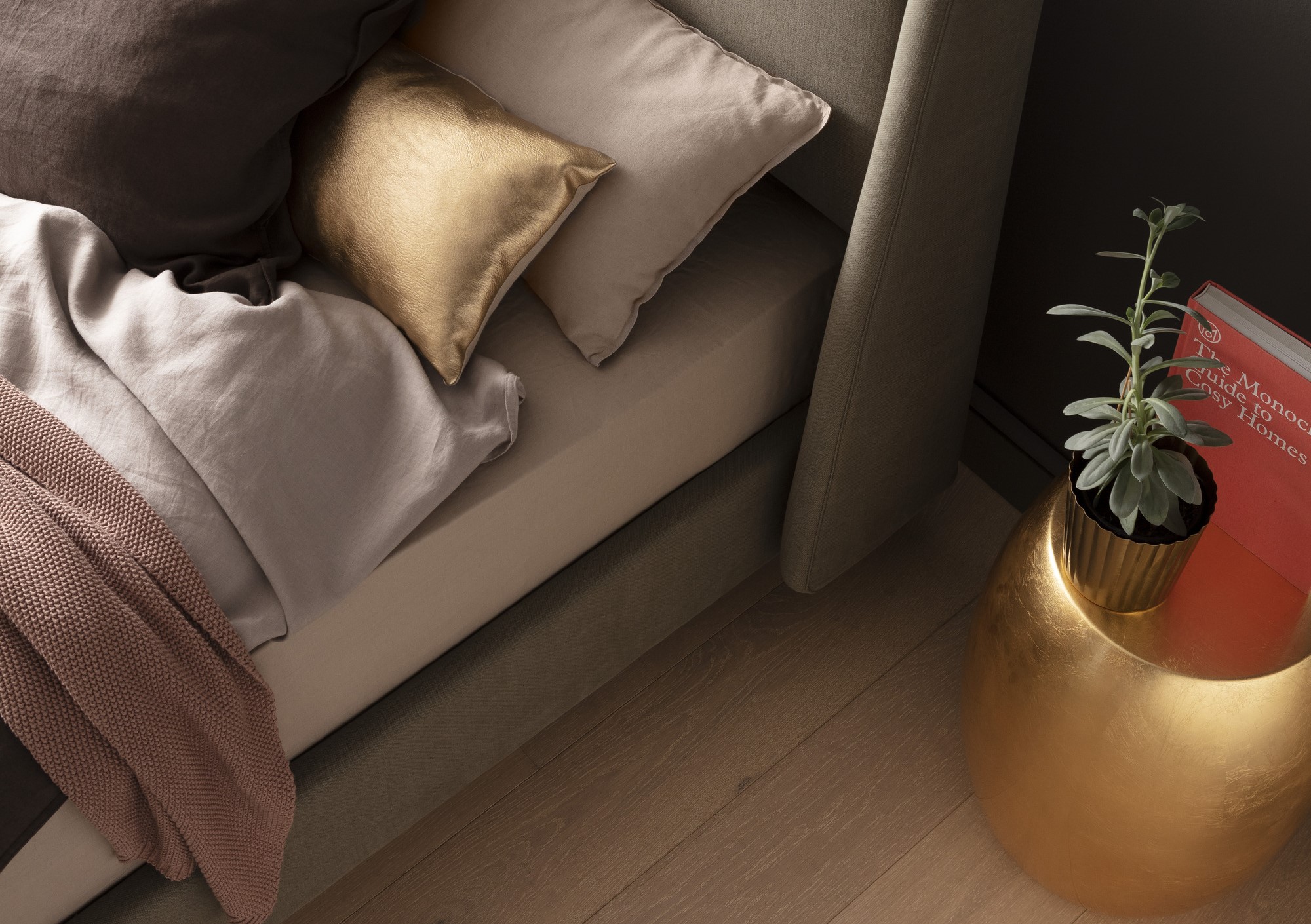 Ein stilvoll eingerichtetes Schlafzimmer mit einem Bett, das mit einem goldenen Kissen, Leinenbettwäsche und einer rosa Decke dekoriert ist. Daneben steht ein goldener Tisch mit einer grünen Topfpflanze und einem roten Buch.