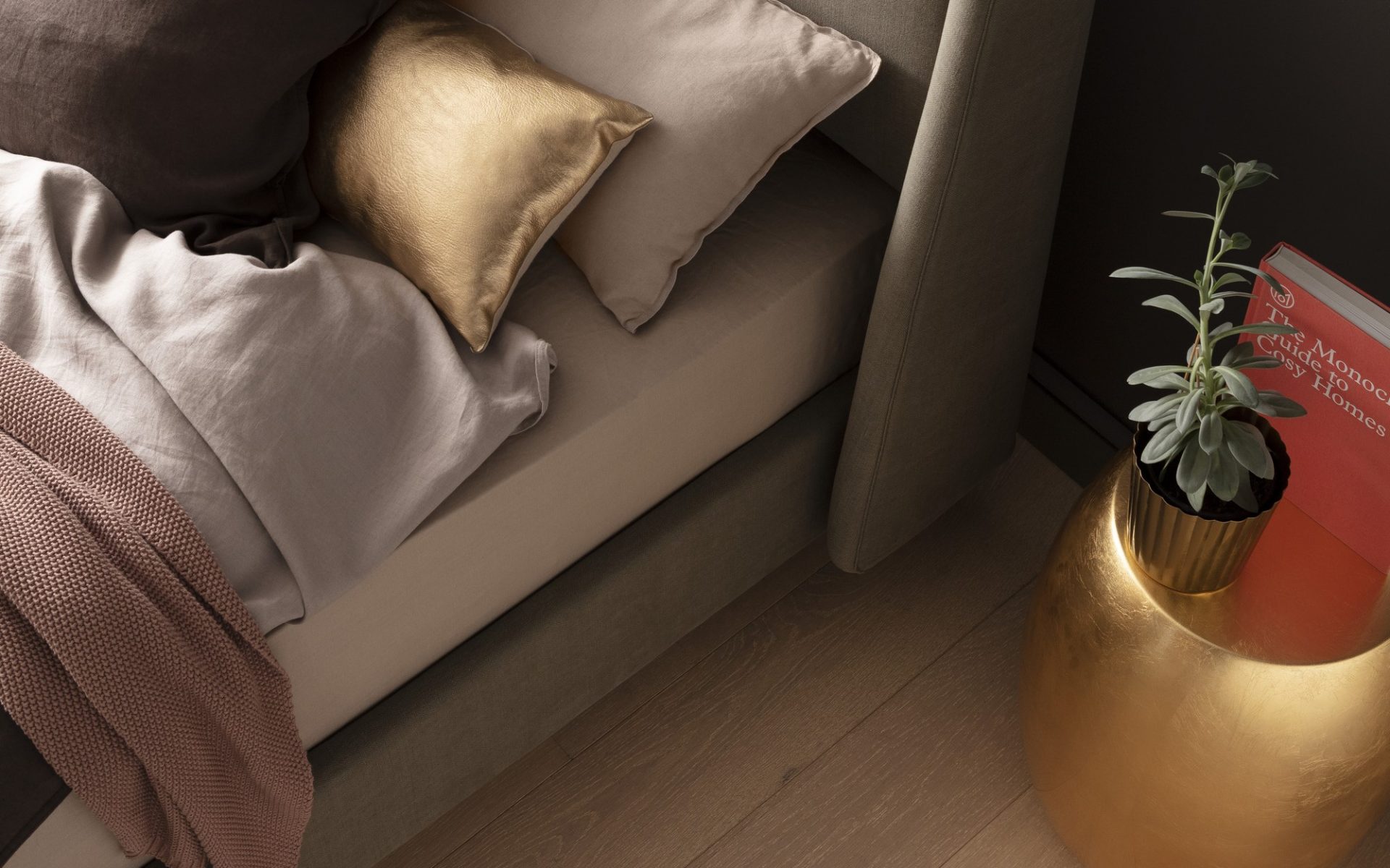 Ein stilvoll eingerichtetes Schlafzimmer mit einem Bett, das mit einem goldenen Kissen, Leinenbettwäsche und einer rosa Decke dekoriert ist. Daneben steht ein goldener Tisch mit einer grünen Topfpflanze und einem roten Buch.